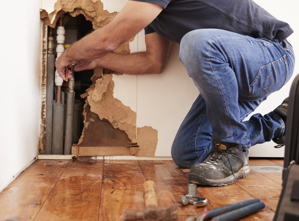 Plumber on emergency service call, fixing a burst pipe in the wall.